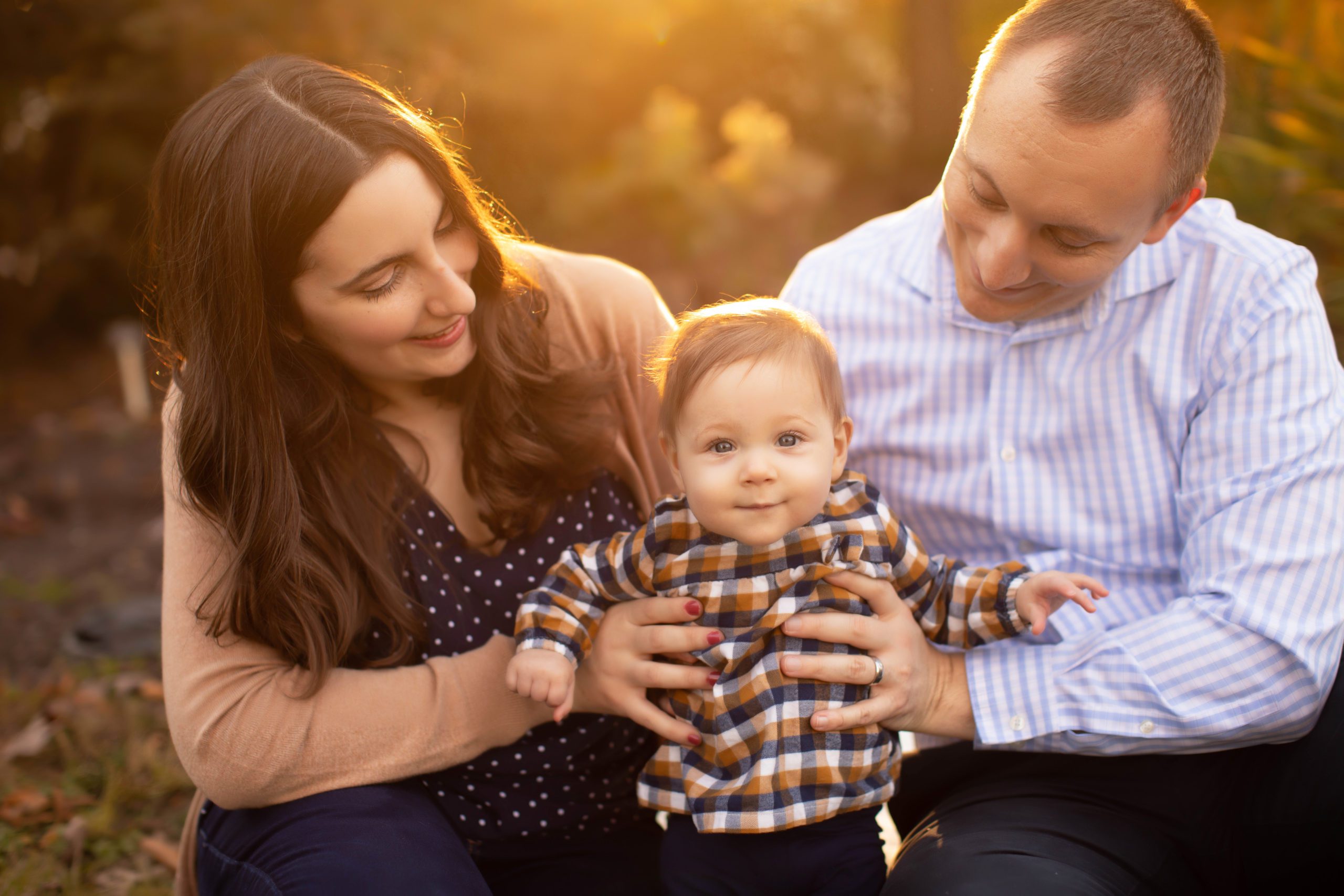 Family sitting in a field of autumn leaves, smiling and embracing during golden hour in Northern Virginia, captured by Marian Lozano Photography.
