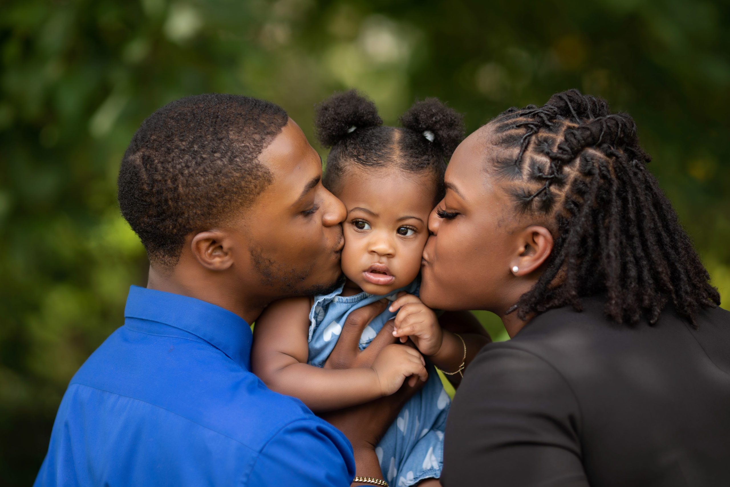 Close up of a sweet moment as mom and dad kiss their baby girl on both cheeks, captured during a natural light family session in Fairfax, VA.