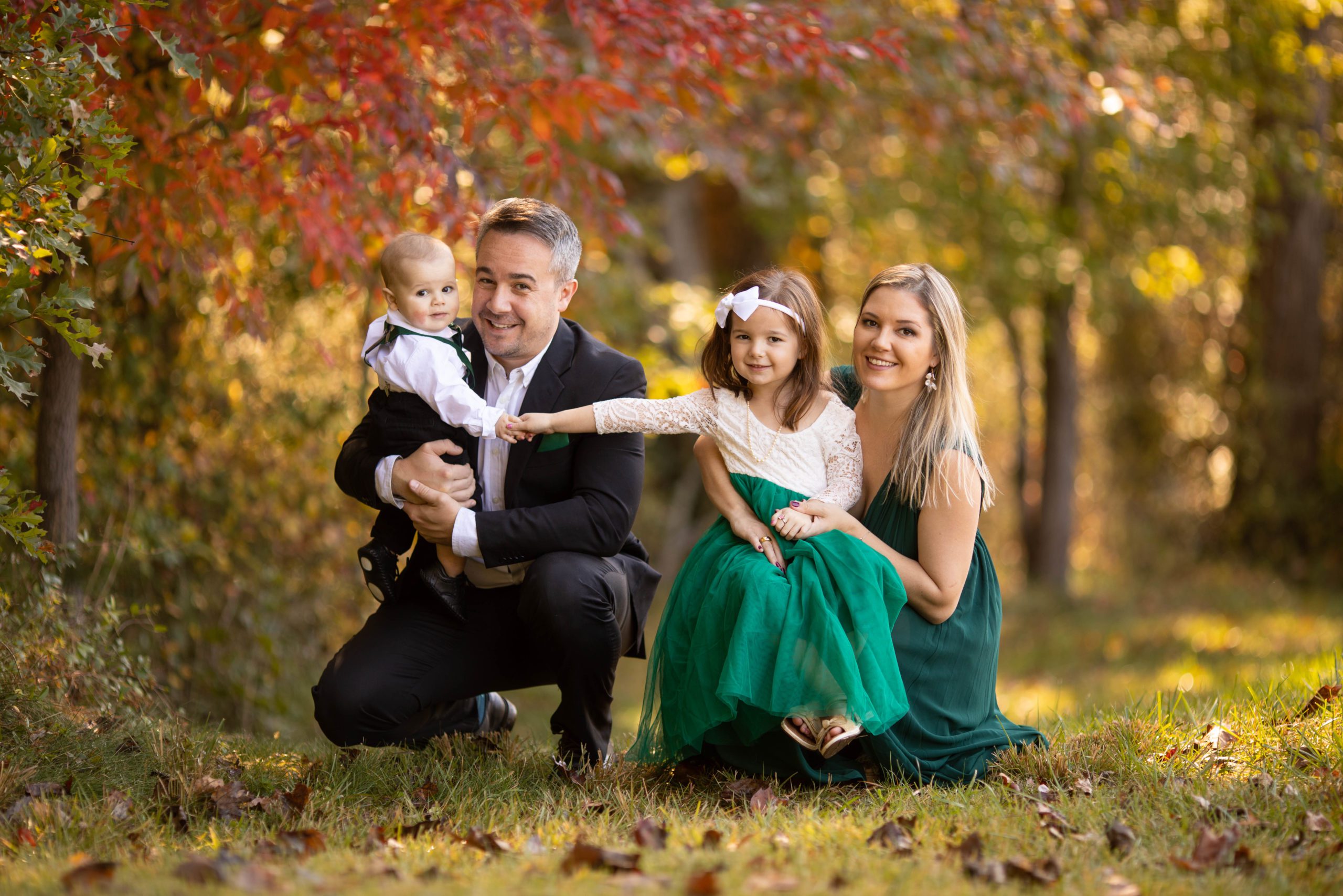 Parents holding their two young children in a vibrant fall setting, surrounded by orange and yellow leaves during a family photo shoot in Northern Virginia.